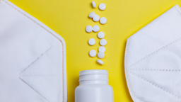 White pills and white pill bottle in between white face masks on a bright yellow background.
ParfonovaIuliia/iStock via Getty Images
