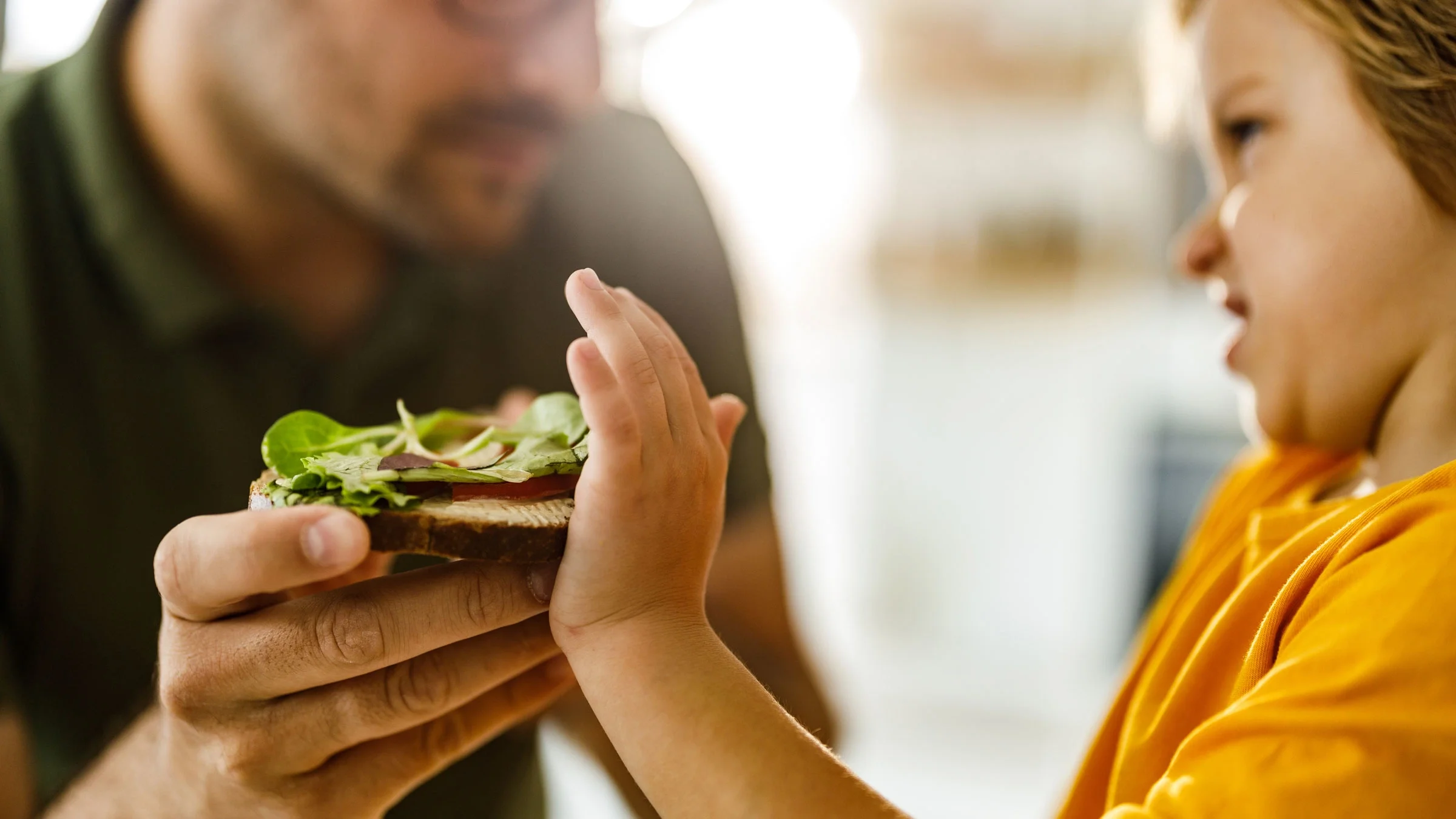 A child refuses to eat a sandwich offered by his dad. People with eosinophilic esophagitis can experience throat pain and trouble swallowing, which can make them not want to eat.