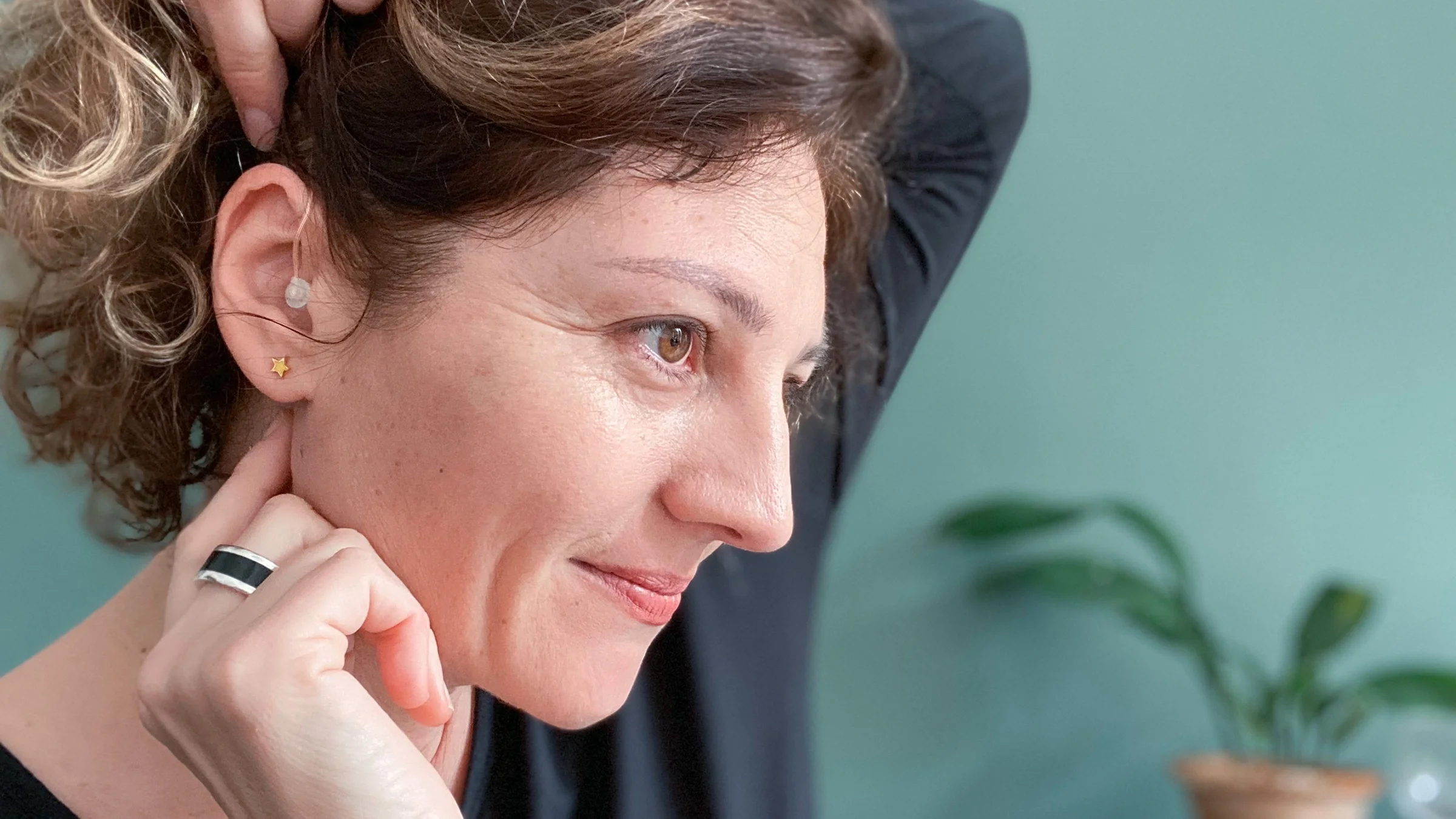 A woman fits a hearing aid in her ear. Over-the-counter hearing aids work for people with mild to moderate hearing loss.