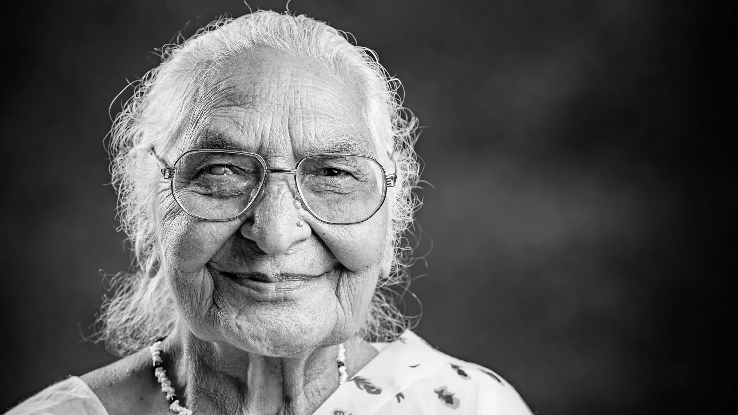 Black and white portrait of a senior woman with glasses. She has a slight smile on her face.