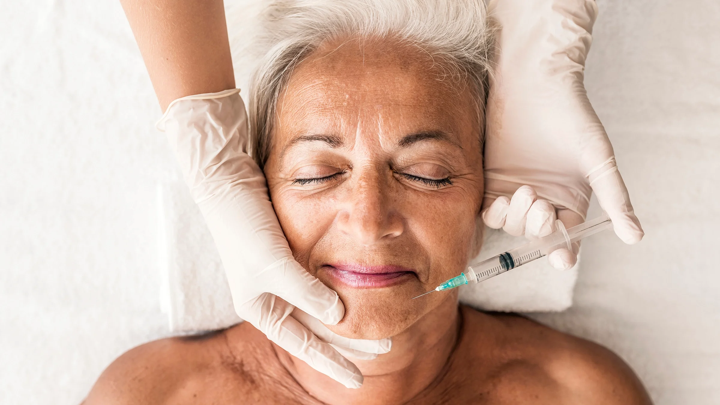 Close-up of a senior woman getting Botox injections. She has her eyes closes and a slight smile on.