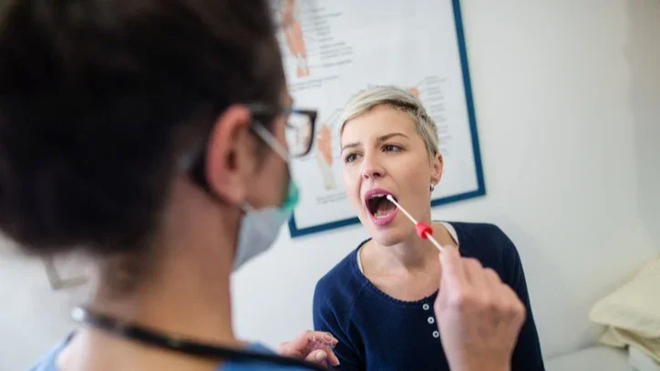 Young woman in the doctors office getting a cheek swab done by the nurse.
dusanpetkovic/iStock via Getty Images