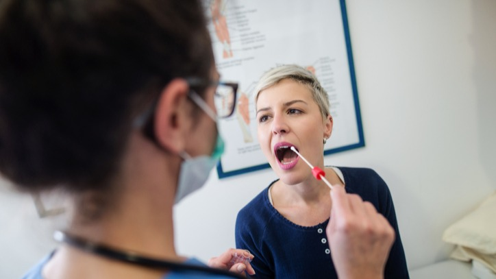 Young woman in the doctors office getting a cheek swab done by the nurse.
