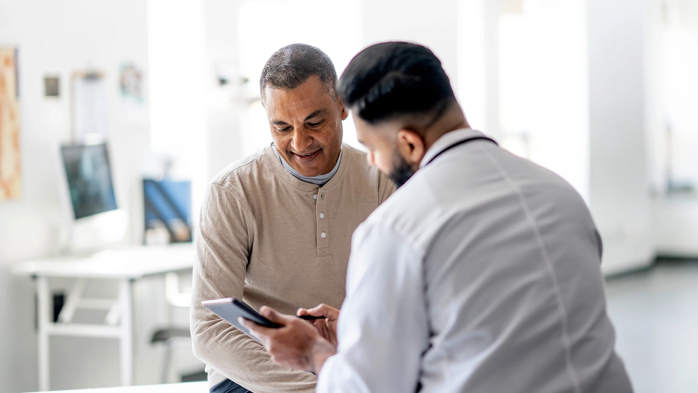A doctor sits across from a male patient and discusses his health at an appointment.