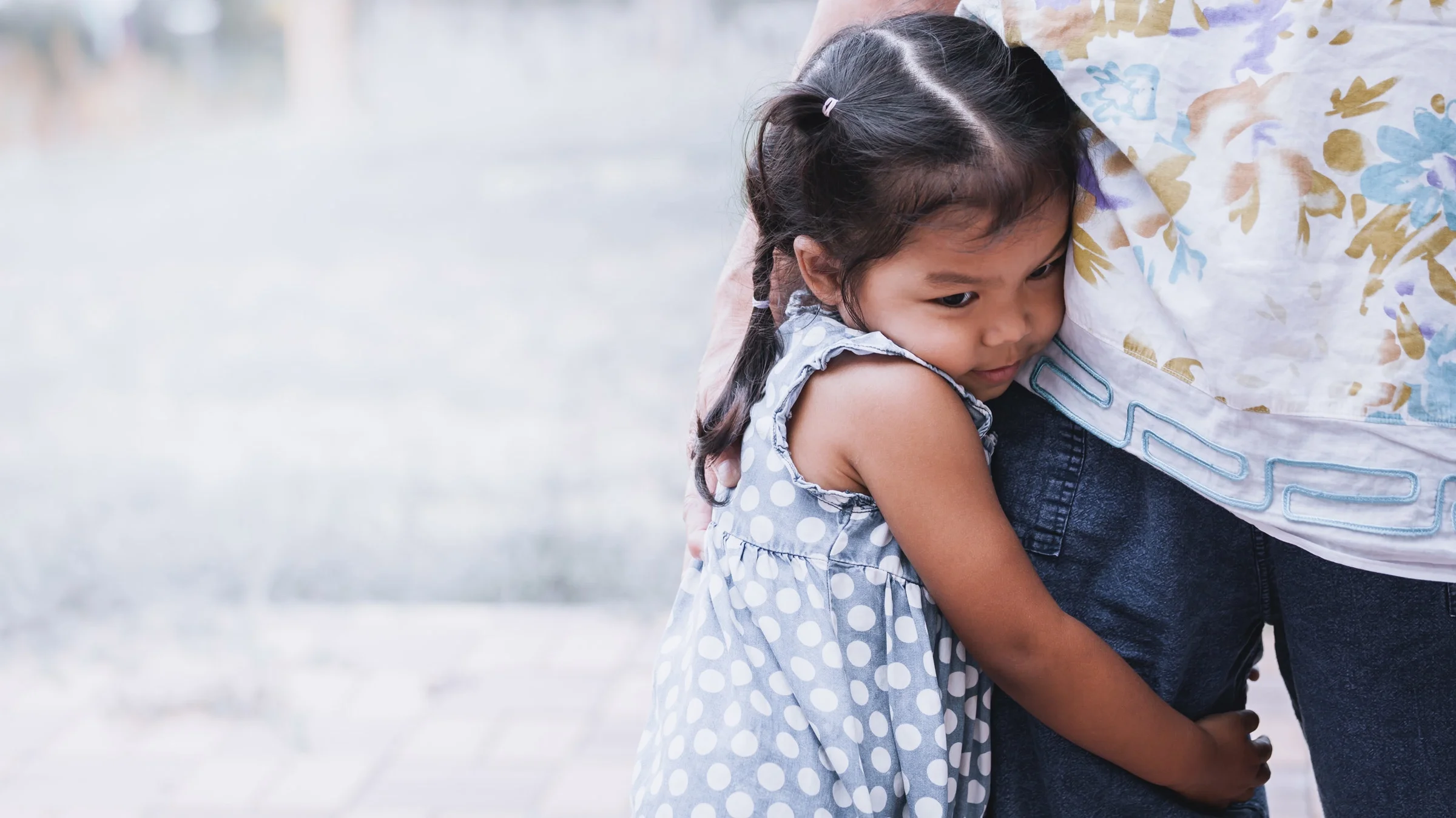 A young child holding tightly onto their parent's leg.