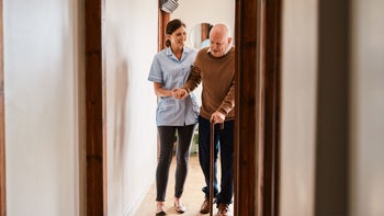 senior-health: woman helps man walk with cane 1184374883