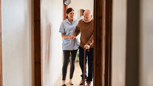 senior-health: woman helps man walk with cane 1184374883