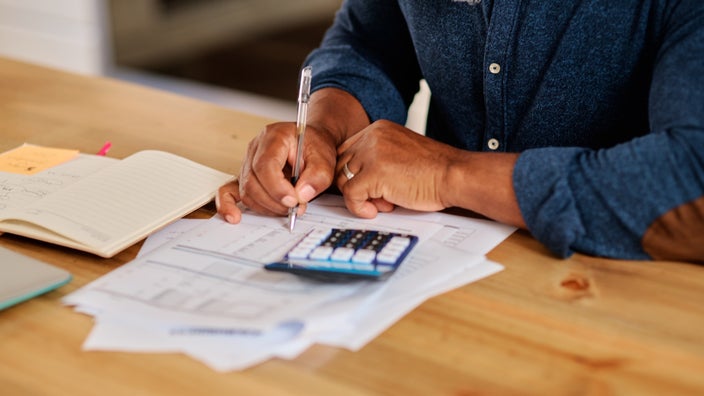 Close-up cropped shot of a man filling out paper work and financial documents with a calculator on the table too.