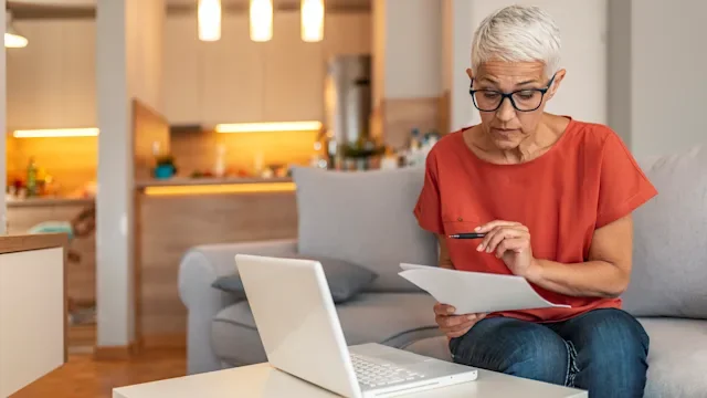 Health: Research: woman reviewing documents with laptop next to her-1169976759