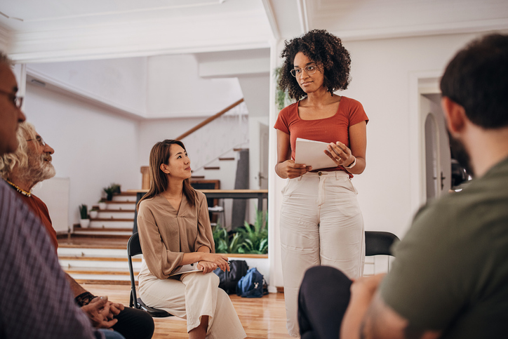 Woman standing up presenting in a work group circled up together.
