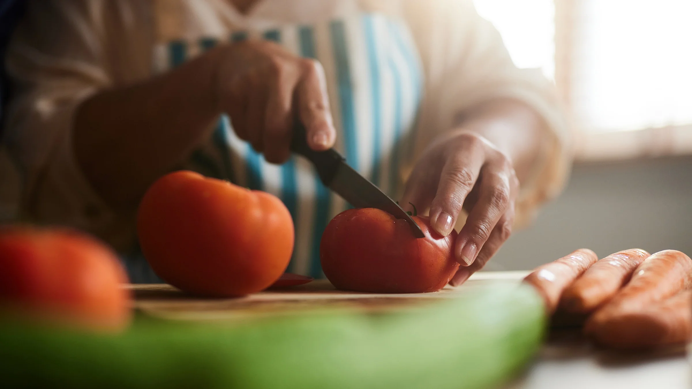 A woman cuts a tomato on a board. 
