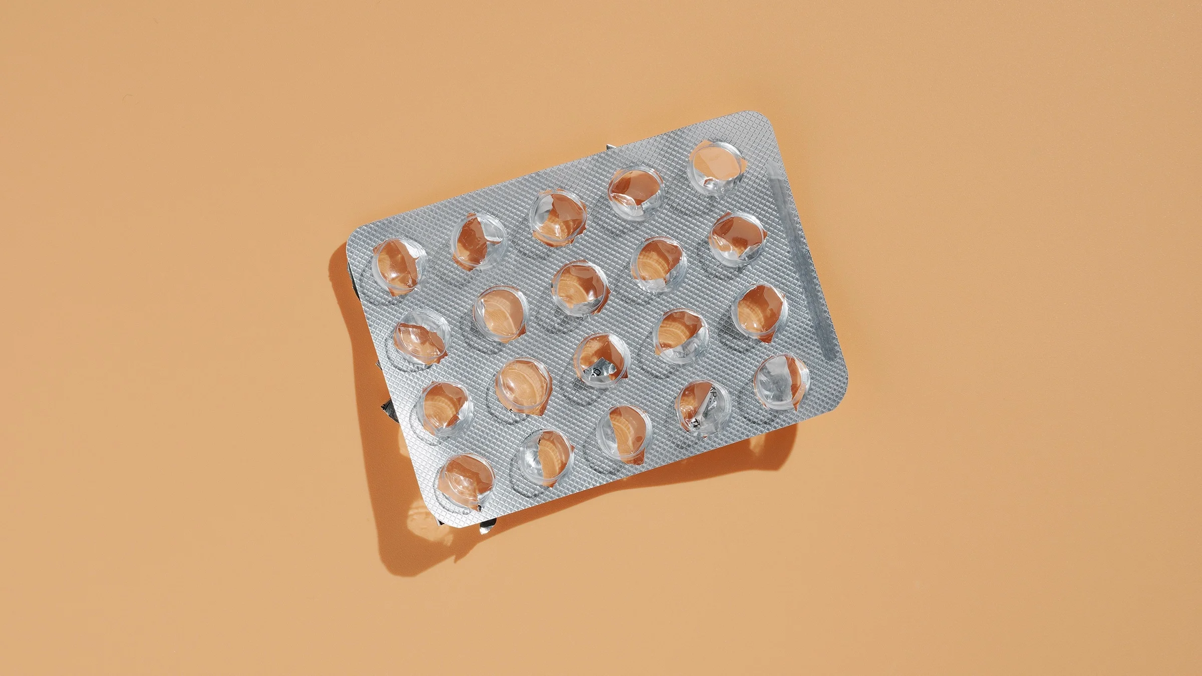 Empty blister pack of pills on a peach colored background.