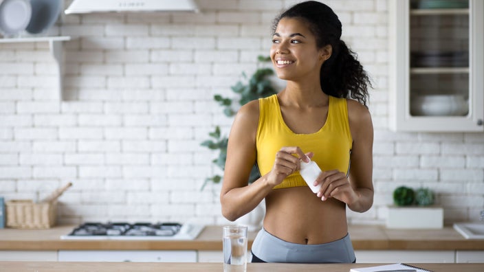 Woman smiling in kitchen holding a bottle of medicine.