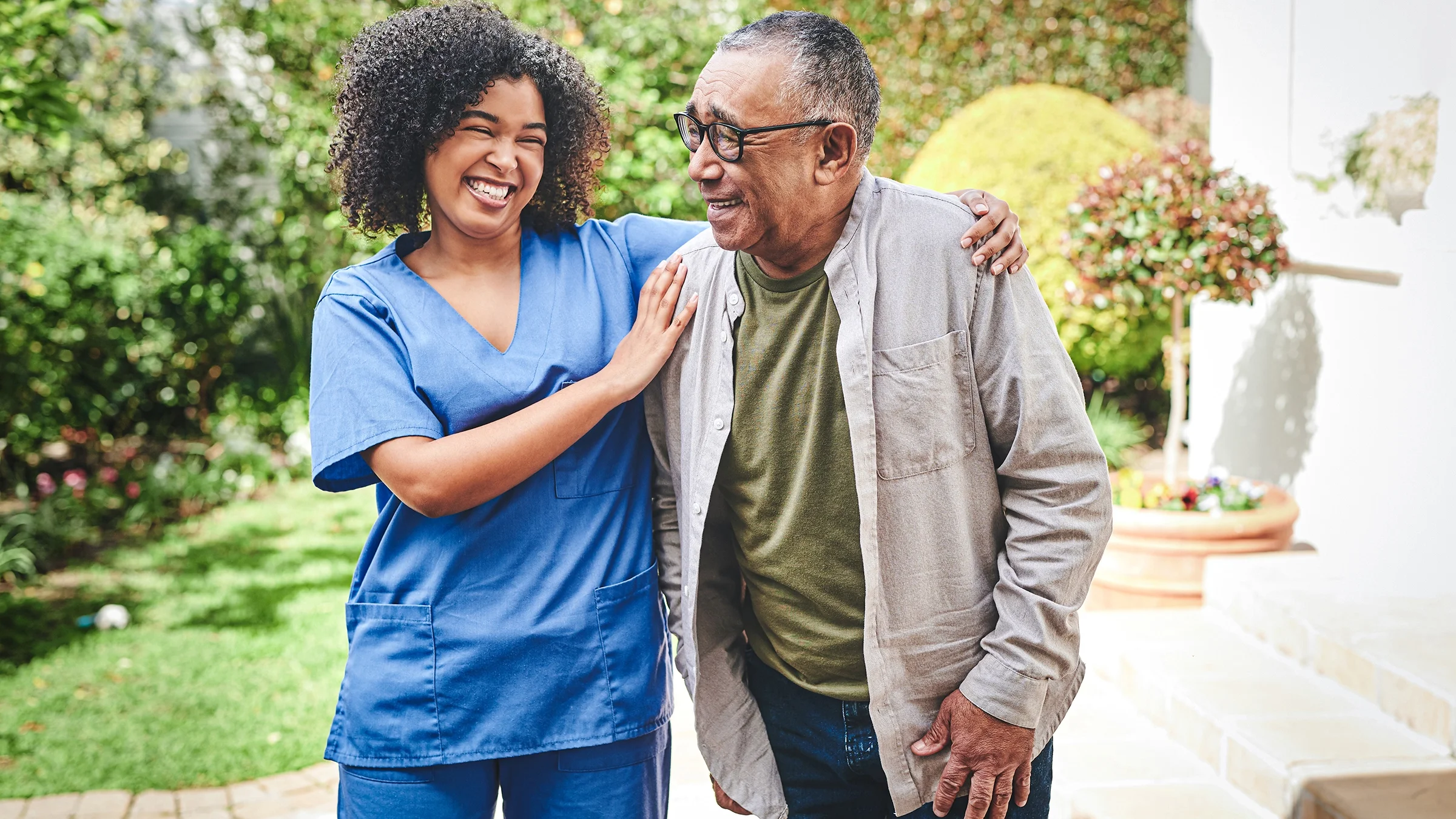 Nurse helping older man walk in courtyard of a senior center.