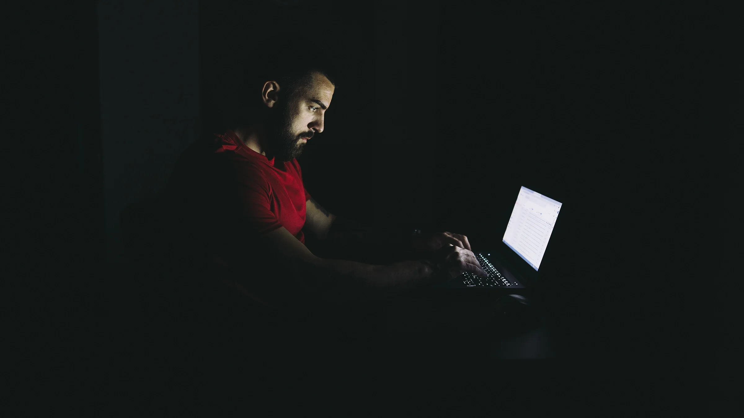Man sitting at laptop in the dark with the computer light lighting up his face.