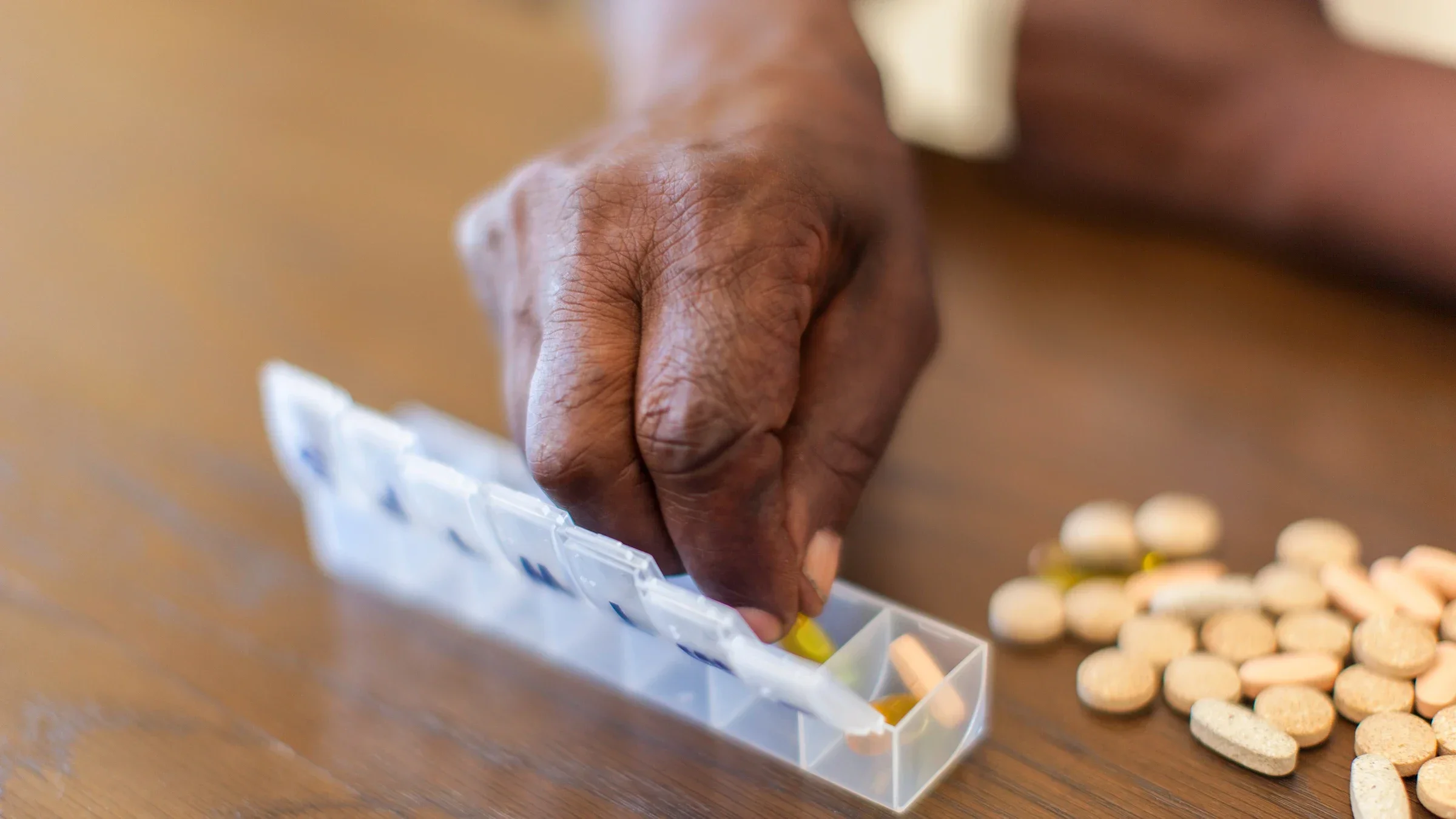 Close-up of an elderly woman's hands placing pills into her daily clear pill organizer with other pills on the table.
AfricaImages/iStock via Getty Images