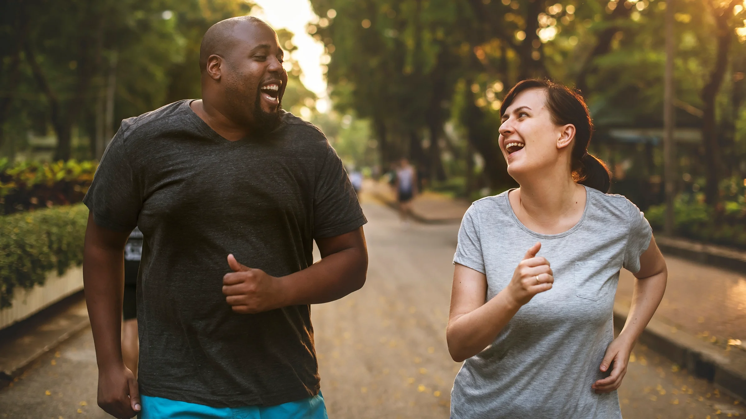 Two friends on a run together. They are looking at each other and laughing.