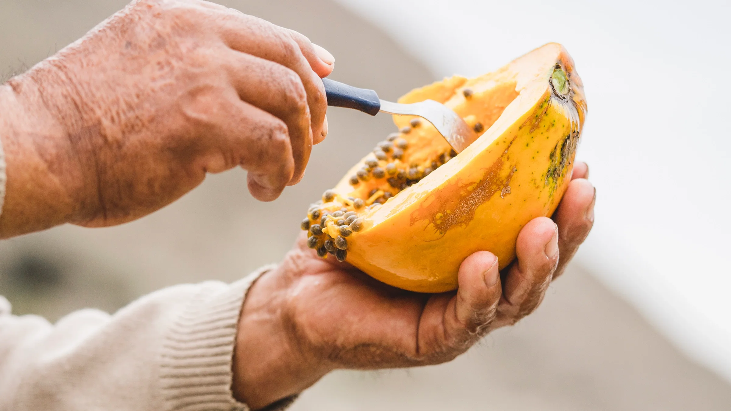 Close-up shot of a senior person scooping out the seeds of a papaya.