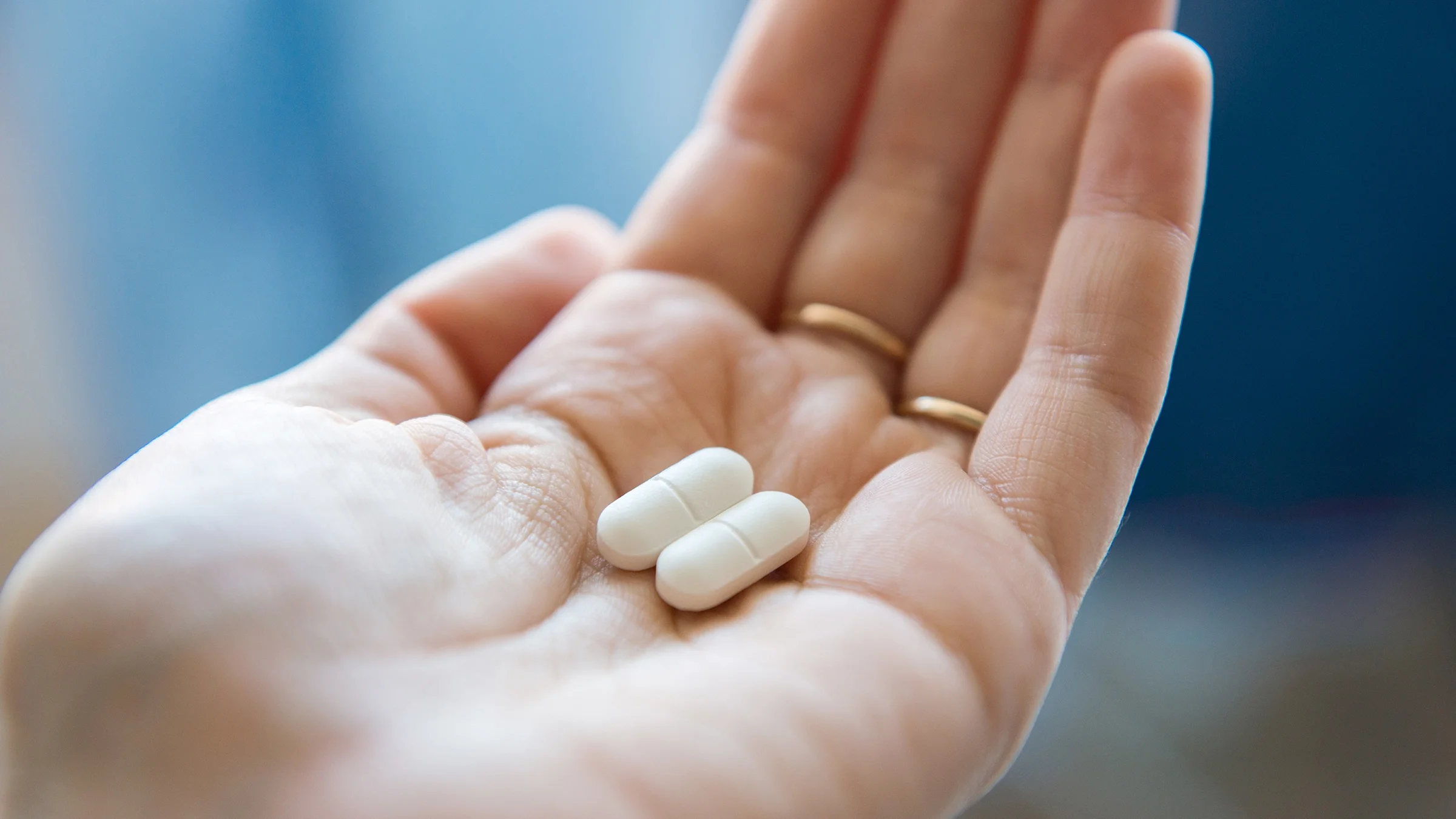  A hand holds two oblong white pills. 