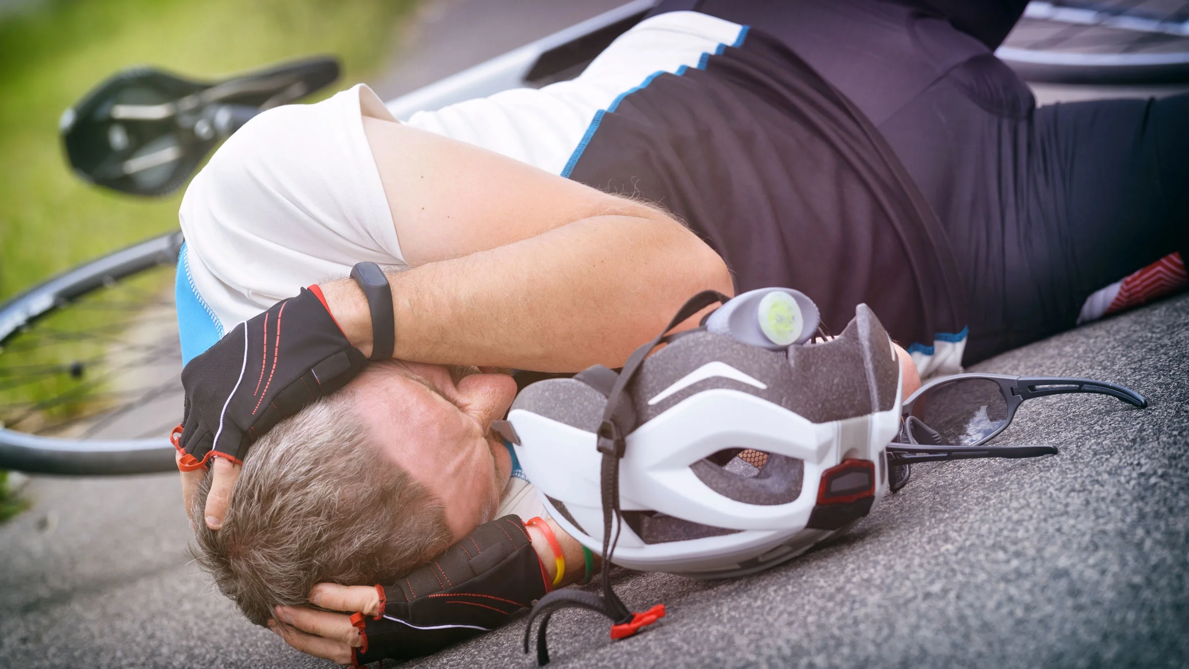 Cyclist lying on the road and holding his head.