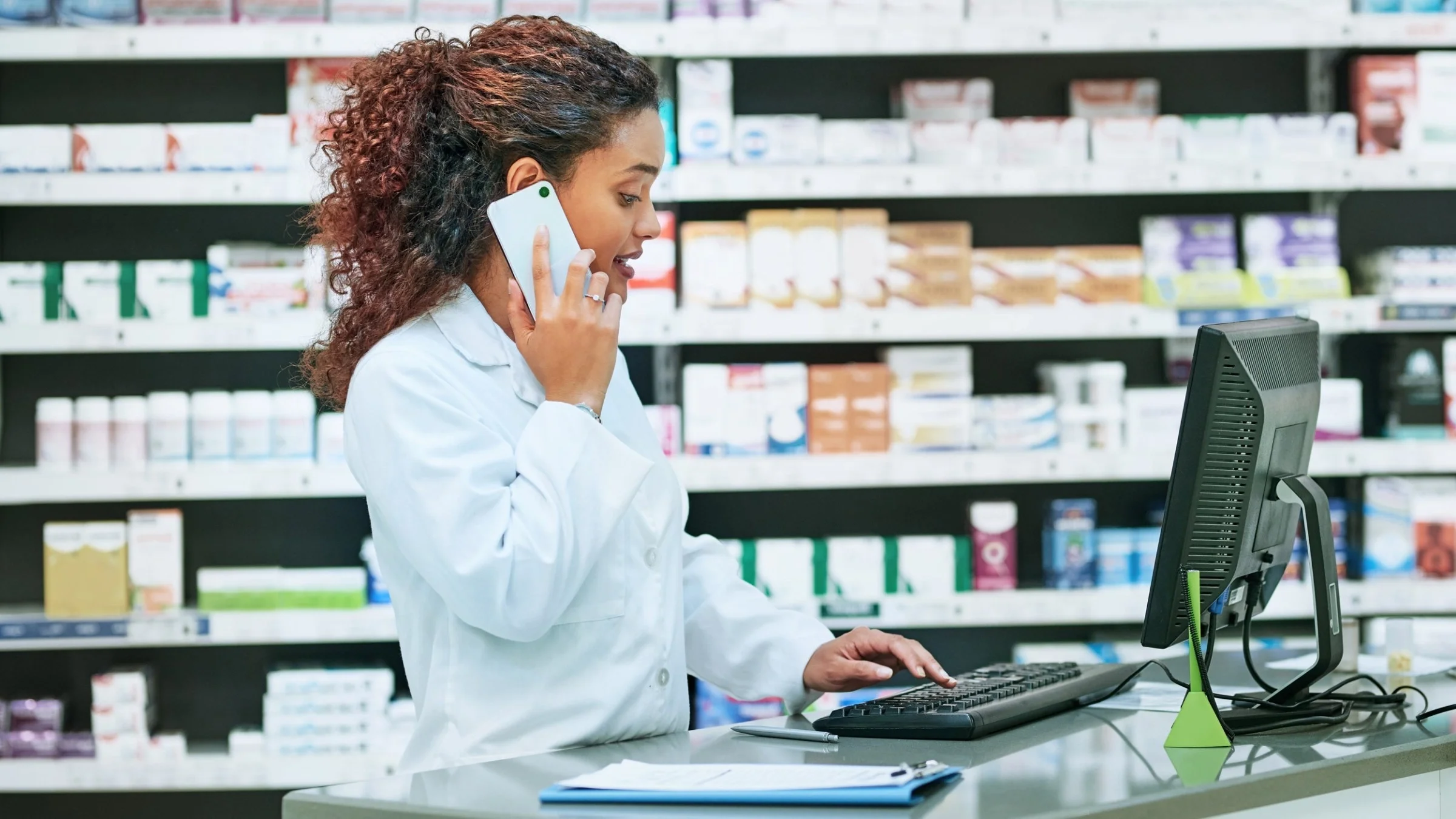 Pharmacist on a phone call and typing on her laptop.