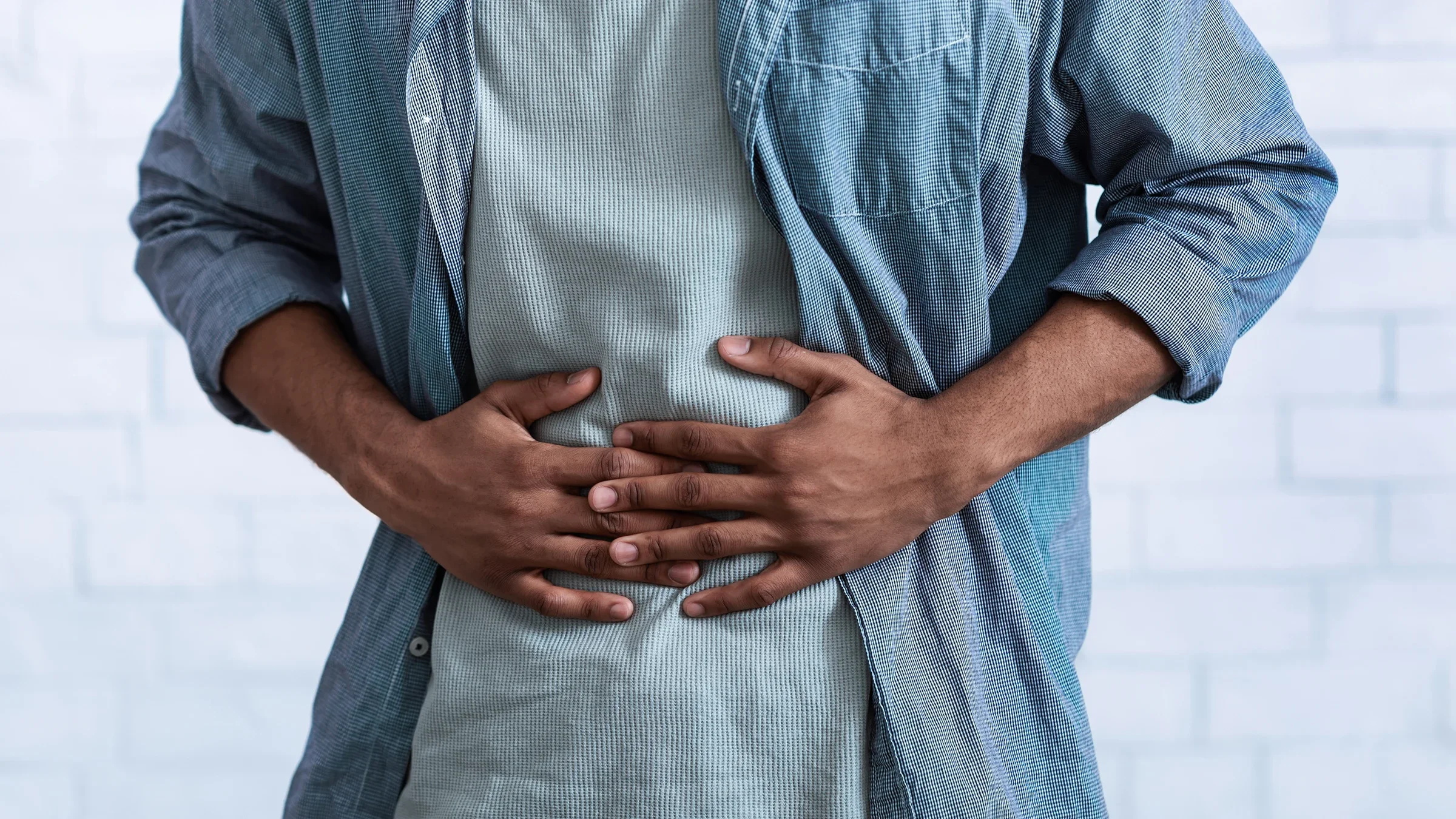 Cropped shot of a man clutching his stomach in pain. He is wearing a button-up shirt over his T-shirt.
Prostock-Studio/iStock via Getty Images