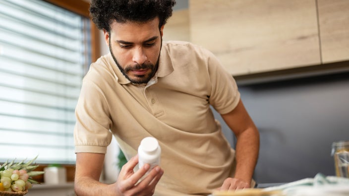 A  man reads the side of a prescription bottle.