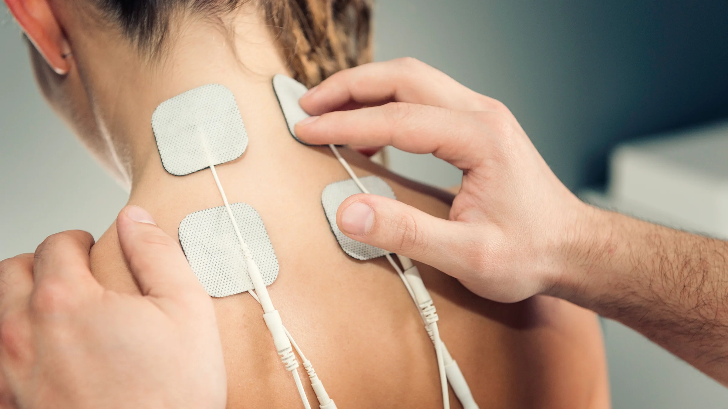 Person applying the TENS device to someone's neck and upper back.