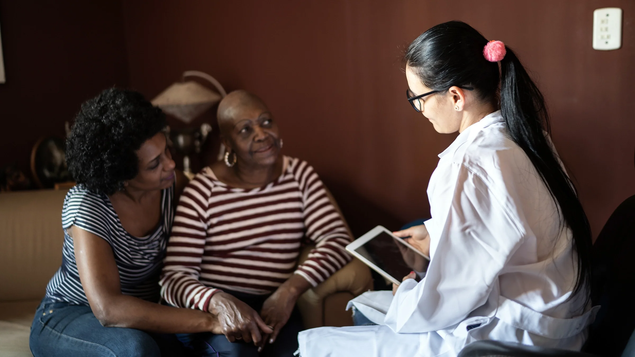 An older woman is comforted by her daughter while talking to a nurse.