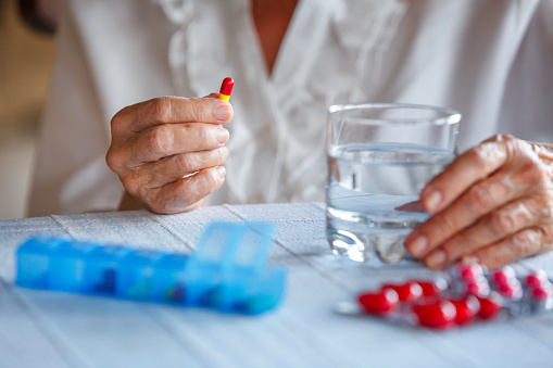 Close-up of an elderly woman taking her pills from a pill organizer at the table.