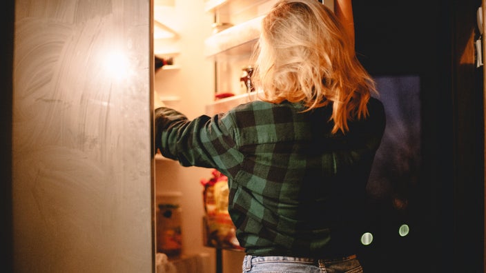 A young adult reaching into a refrigerator to get something.