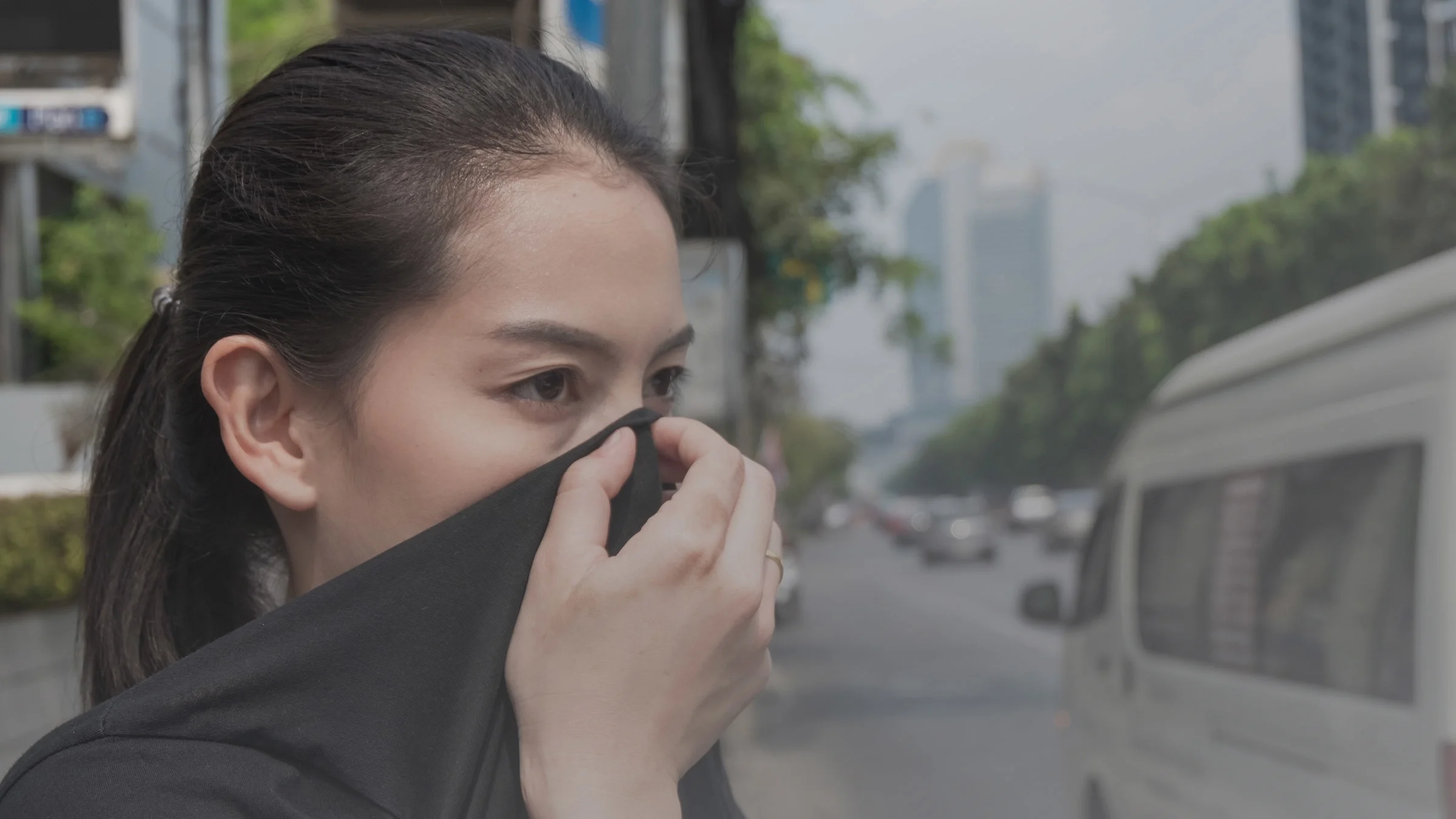 A woman covering her nose with her shirt in a polluted city.