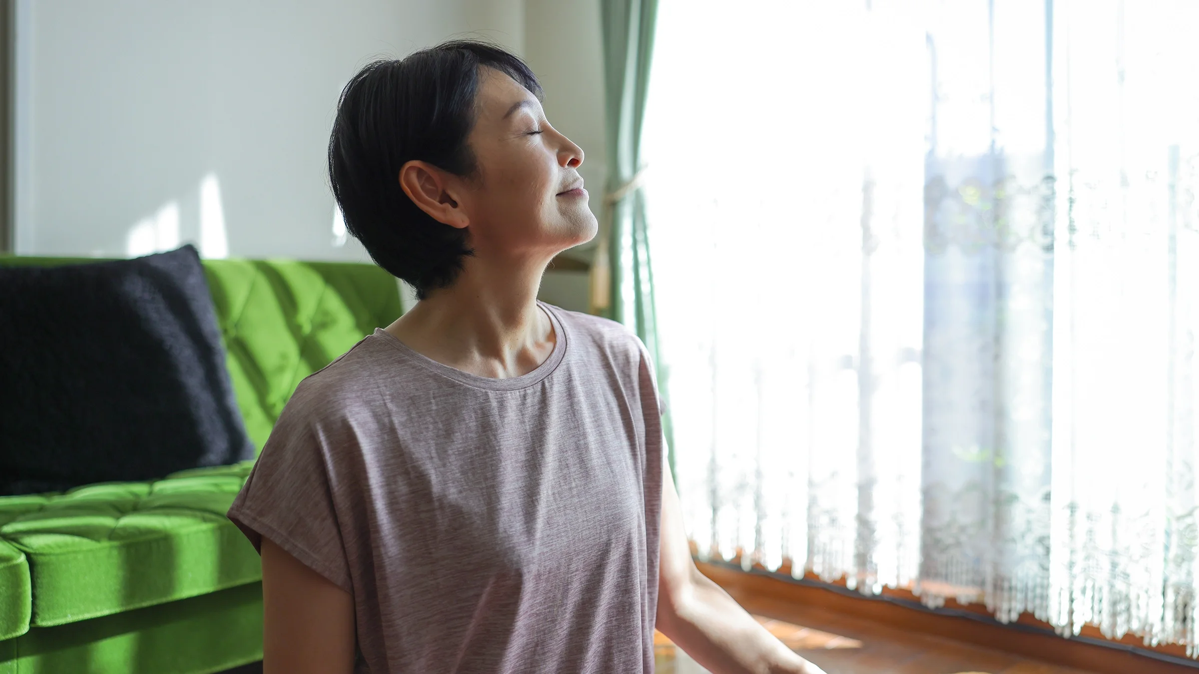A woman feels the warmth of sunlight coming through the window.