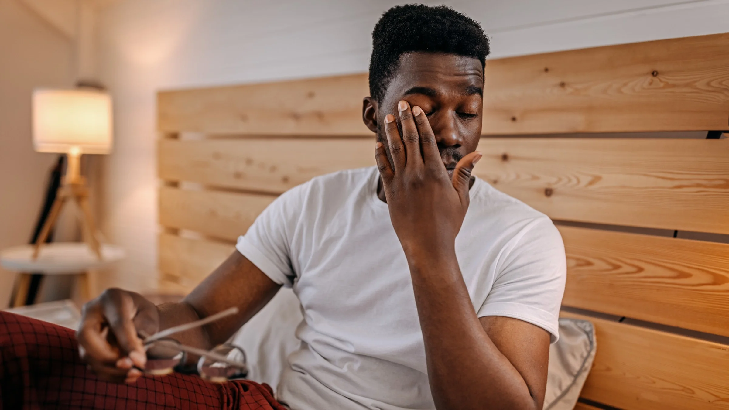 Man waking up in the morning and rubbing his eyes before he puts on his glasses.