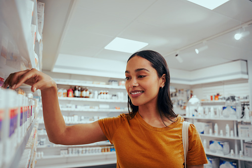 Portrait of smiling young woman in drugstore picking medicine.