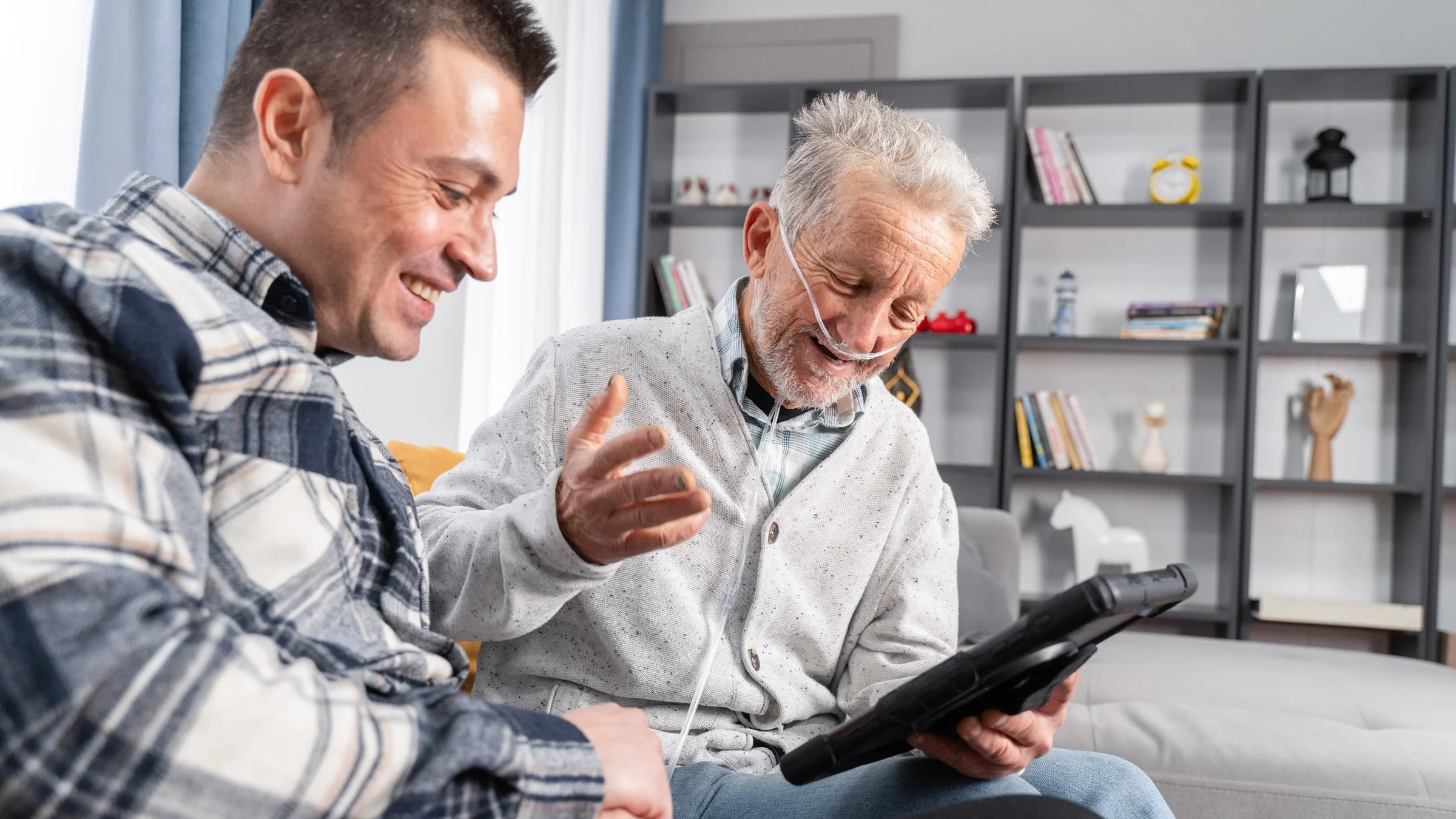 A man using a portable oxygen concentrator looking at a tablet with his son.