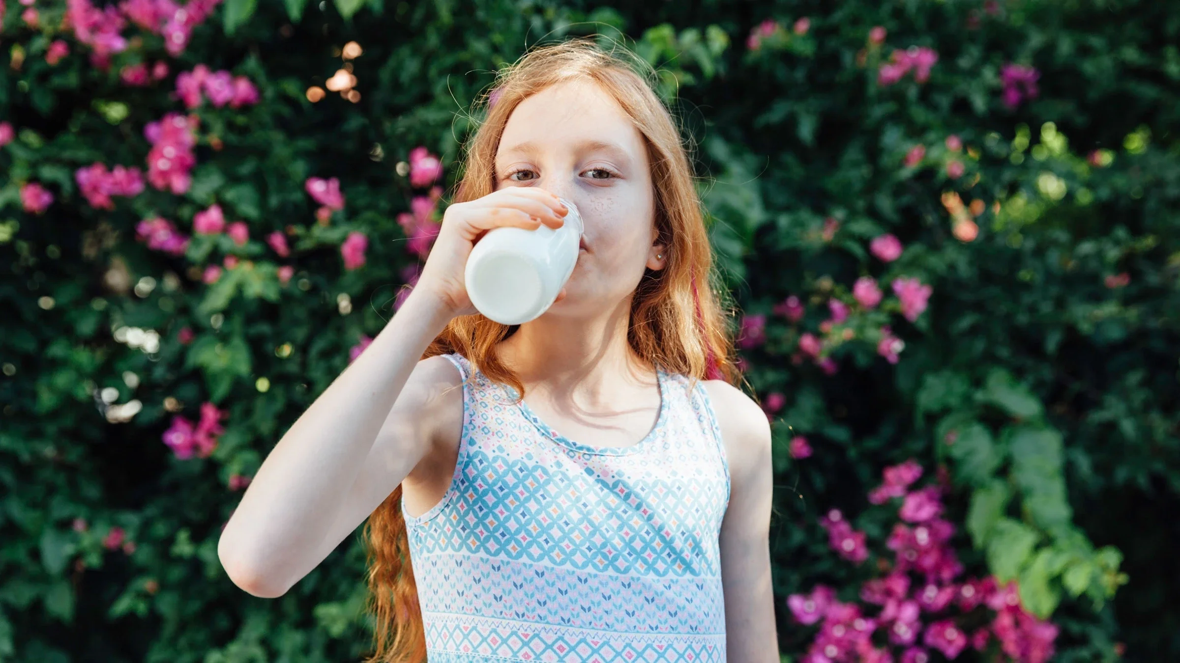 A young child drinking milk in a flower garden.