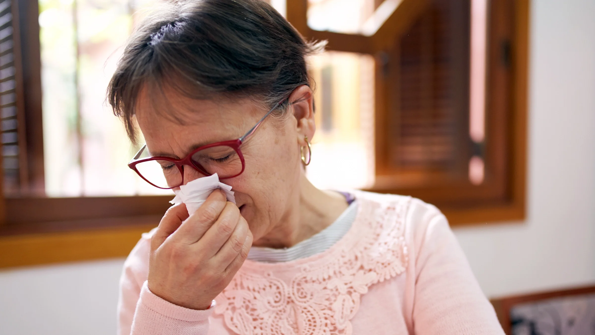 Woman sneezing into a tissue.