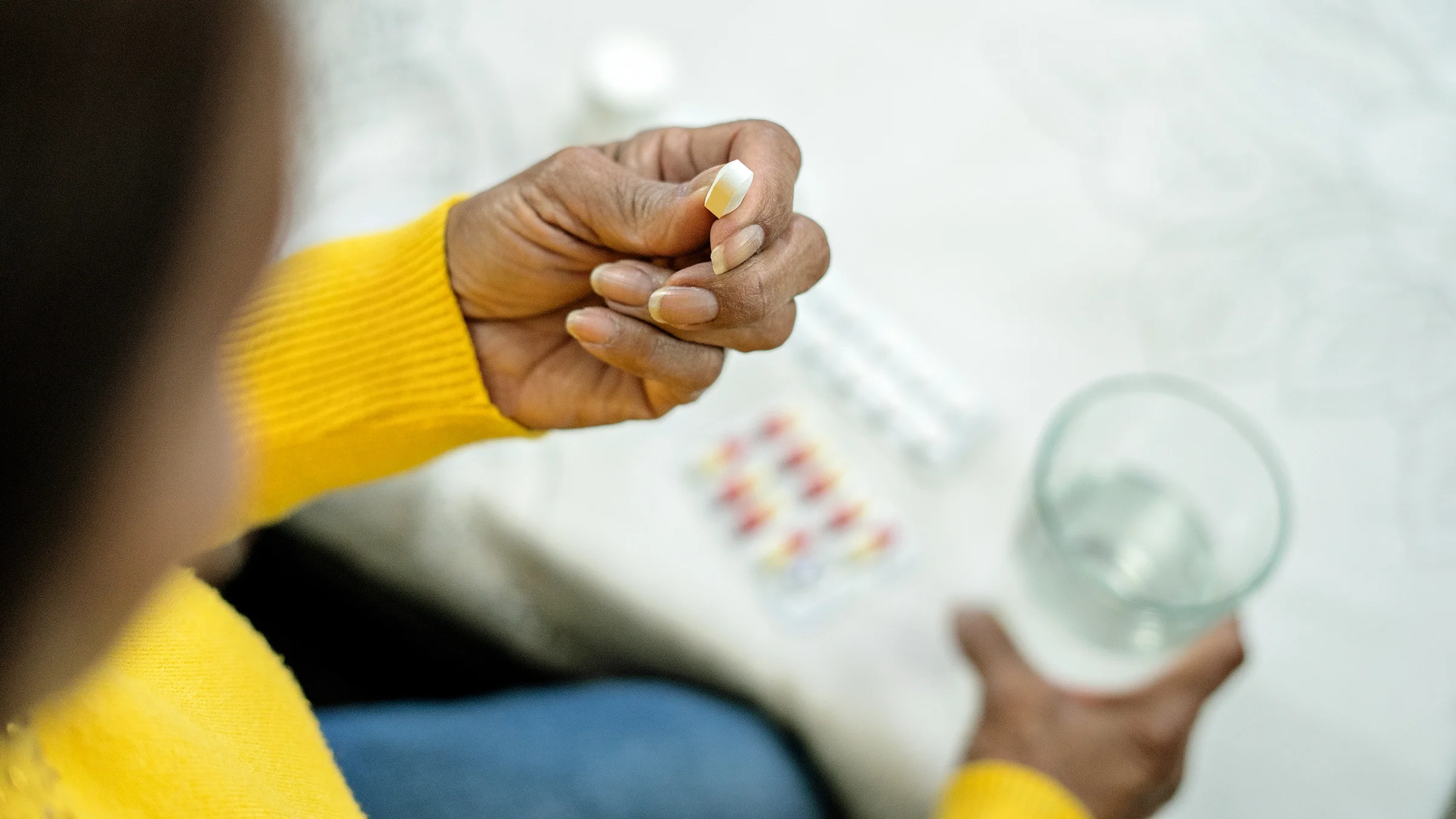 Close-up of a pill in a hand and a glass of water.