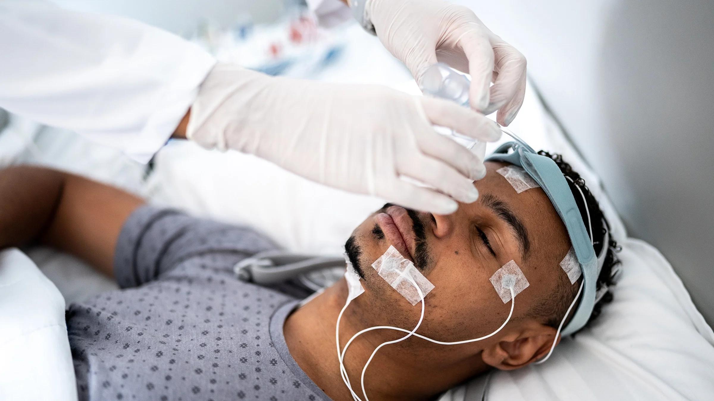 Doctor setting up a sleep study on a man laying down.