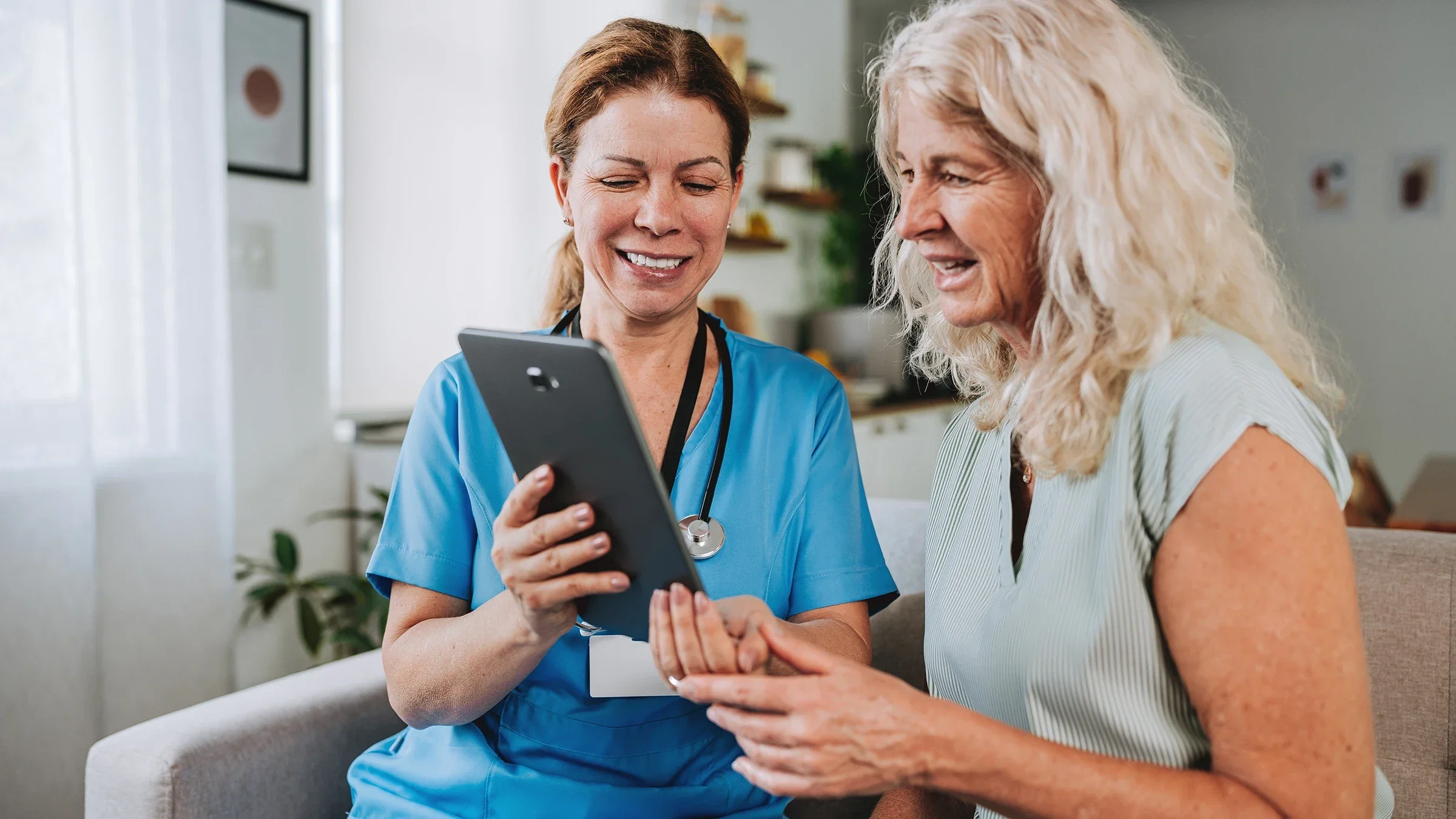 A healthcare professional shows a woman something on a tablet during a home visit.
andreswd/E+ via Getty Images