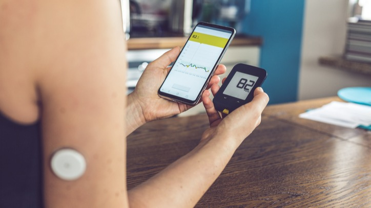 Close-up of a woman using a glucose monitor with her smart phone to see the reading. She also has a glucose sensor in her arm.