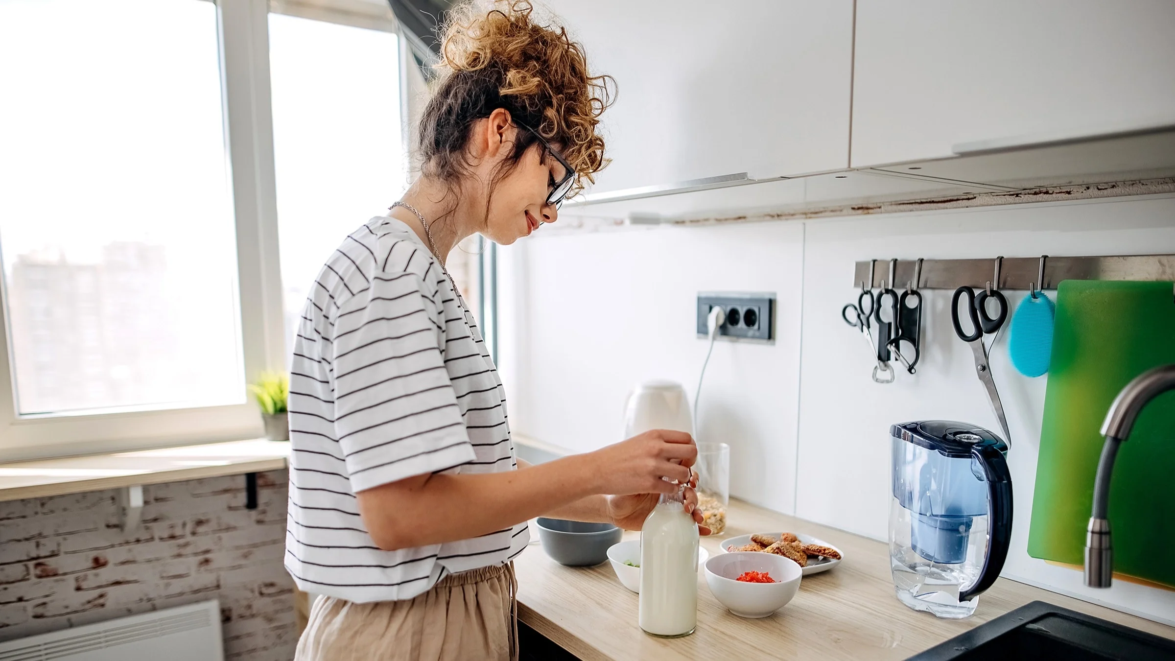 A young woman with her hair tied up in a curly bun preps her breakfast with milk.