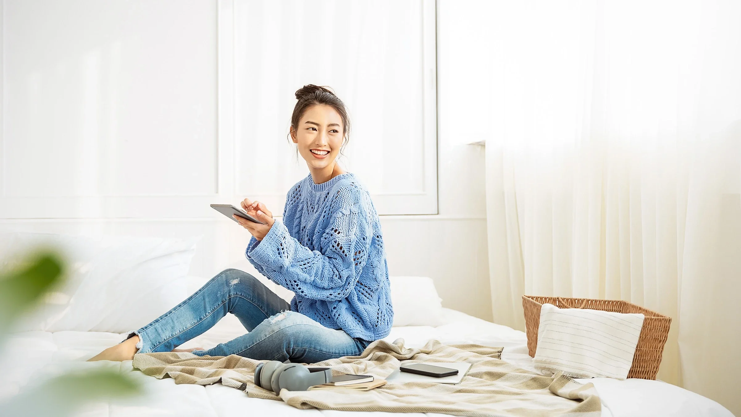 Woman sitting on her bed using a tablet and smiling.