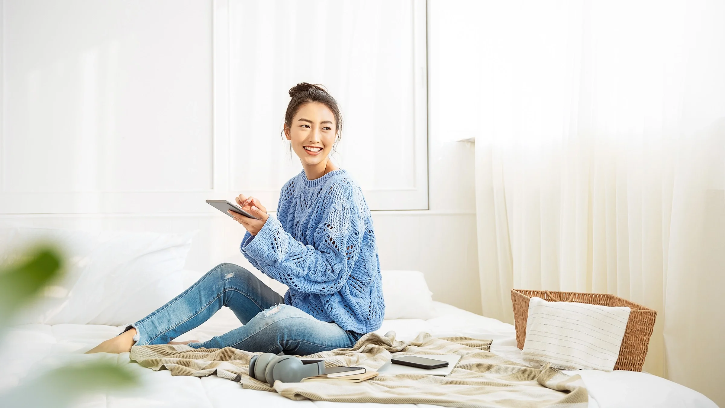 Woman sitting on her bed using a tablet and smiling.