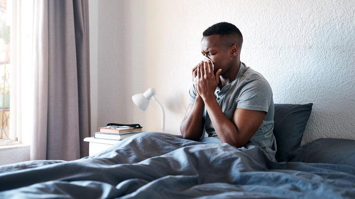 A man sitting in his bed blows his nose.