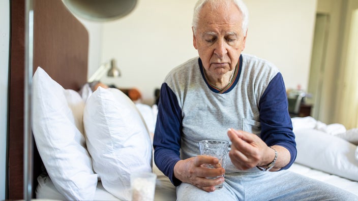 A man sitting on the edge of his bed prepares to take his prescription medication.