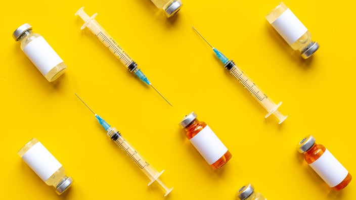 Vaccine vials and syringes on a bright yellow background creating a diagonal pattern.