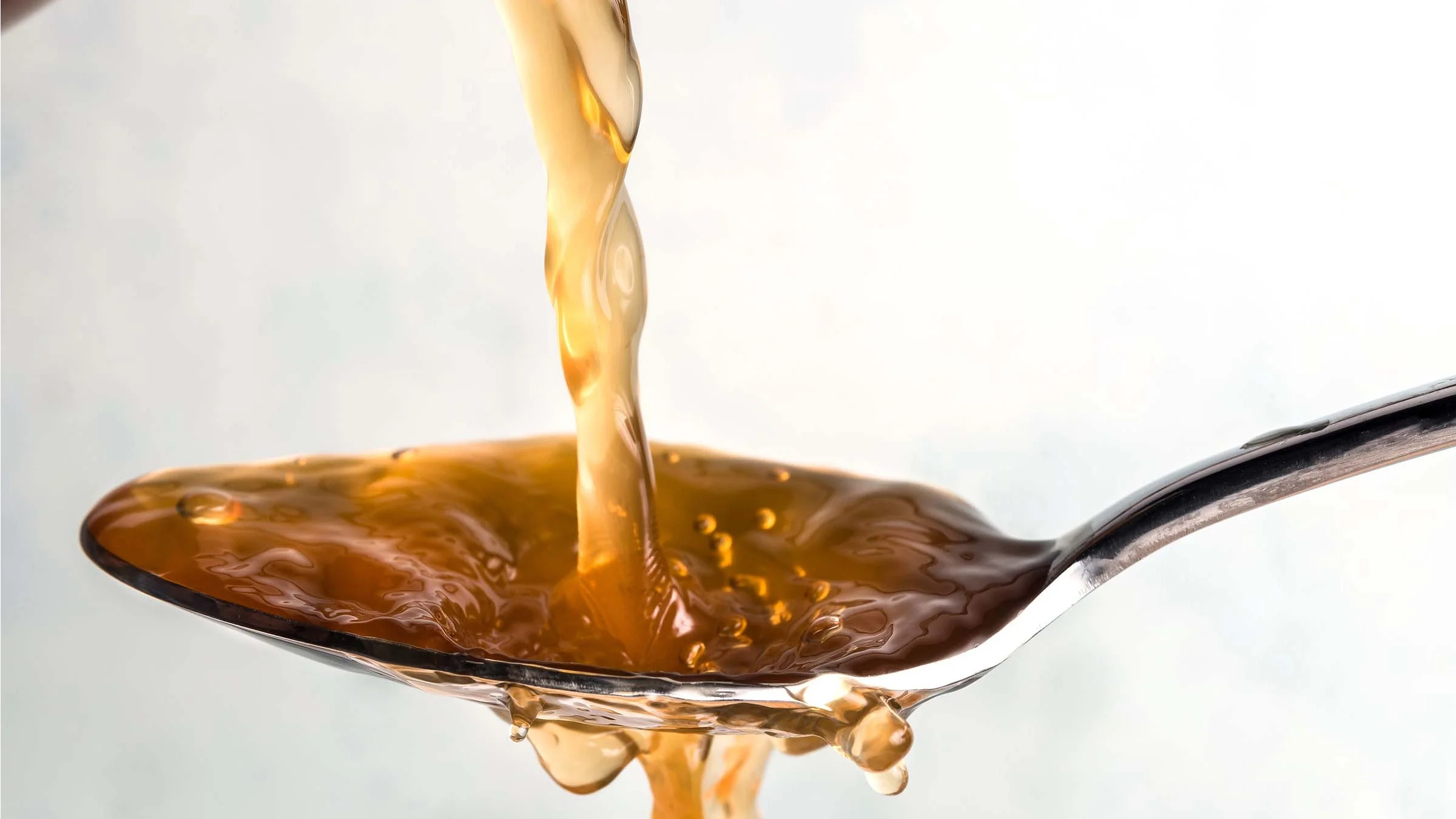 Extreme close-up of apple cider vinegar being poured on to a spoon and overflowing.