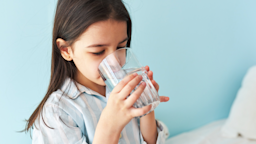 Young little girl drinking a glass of water in her striped pajamas.
Yuricazac/iStock via Getty Images